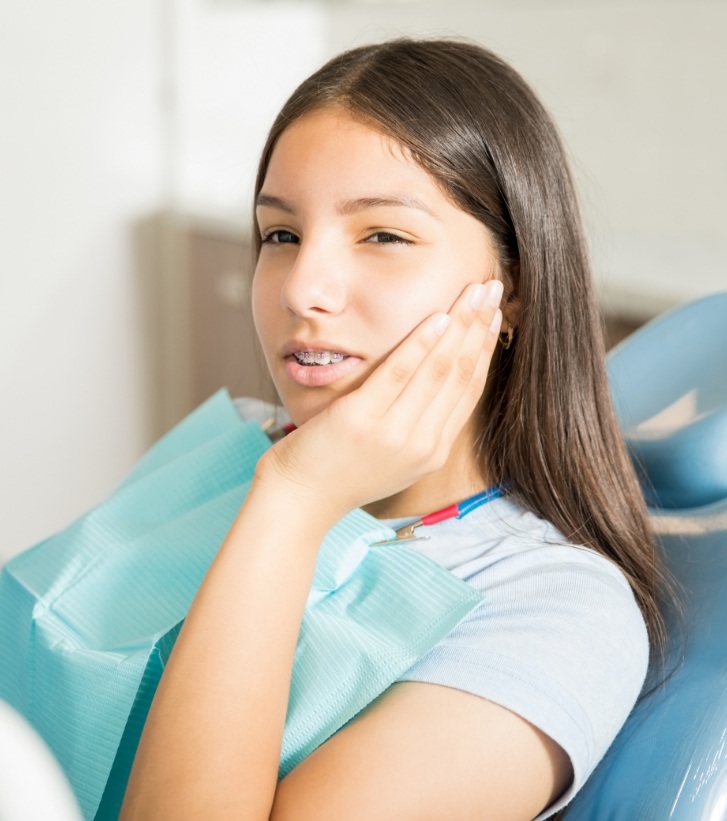 Young woman in dental chair holding her cheek in pain