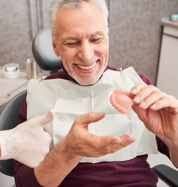 Smiling man in dental chair holding a denture