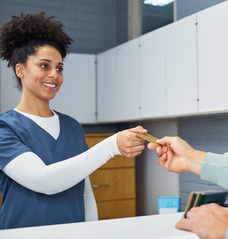 Woman in scrubs accepting payment card from man in pale sweatshirt
