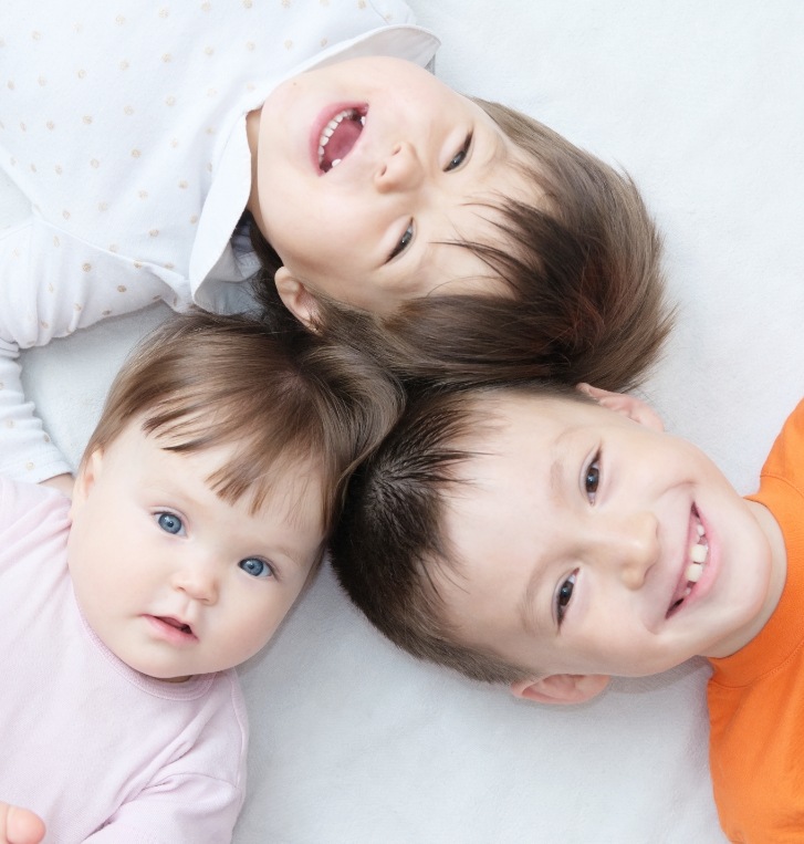Three smiling children laying on the floor