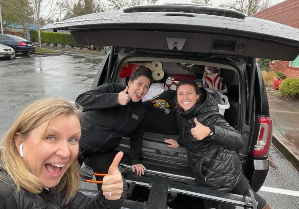 Dental team members giving thumbs up next to car filled with gifts to donate