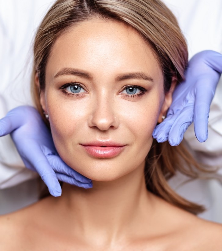 Woman in dental chair with gloved hands gesturing toward her face