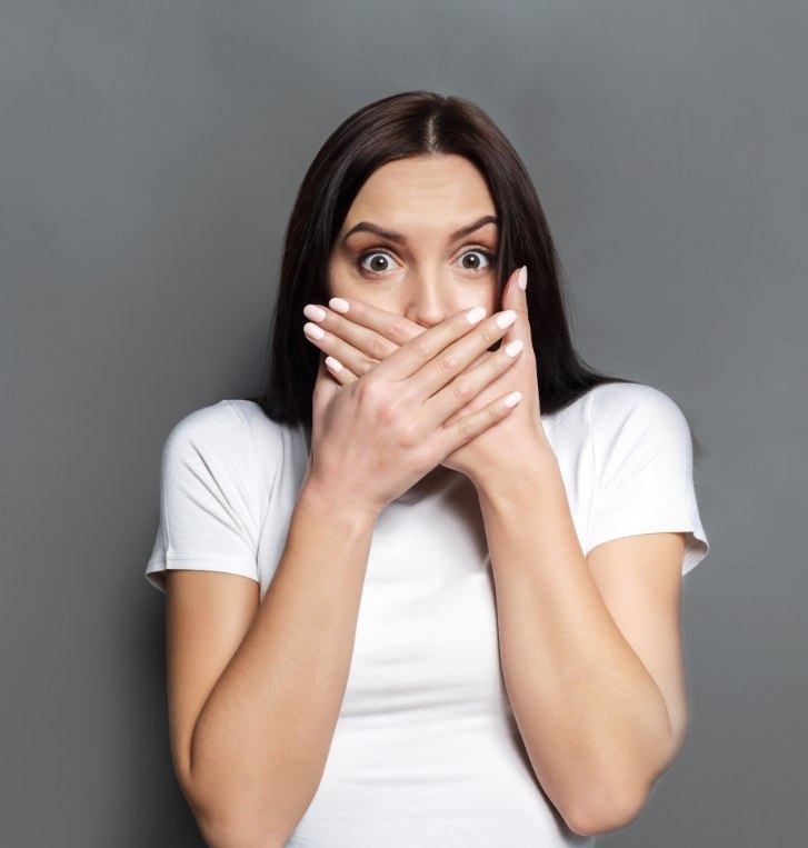 Woman with raised eyebrows covering her mouth with both hands