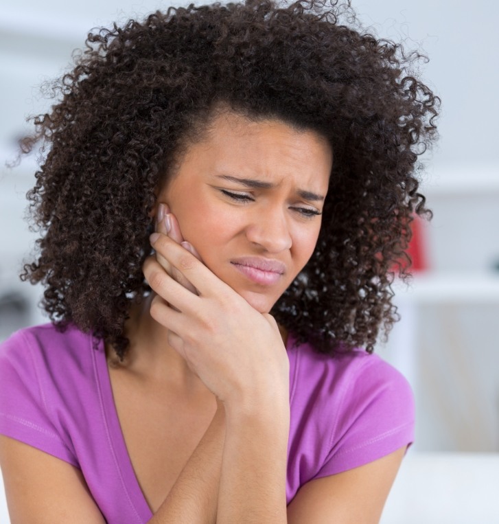 Woman wincing in pain while holding her cheek