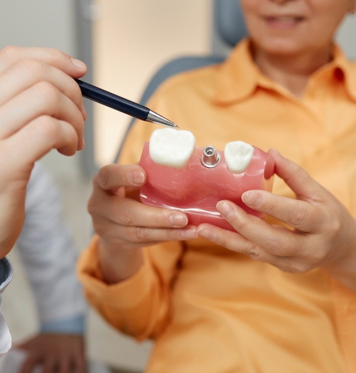 Dentist showing a patient a model of the jaw with a failed dental implant