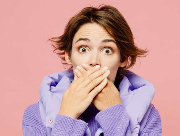 Woman with raised eyebrows covering her mouth with both hands