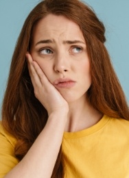 Woman in yellow blouse holding her cheek in pain