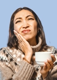 Woman with coffee mug holding her cheek in pain