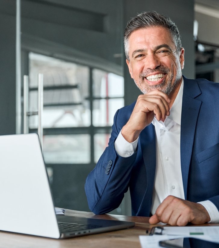 Smiling businessman sitting at desk with laptop