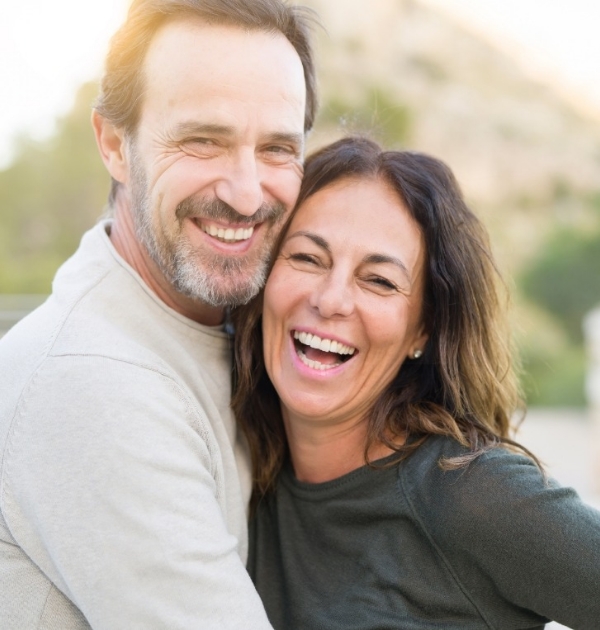 Man and woman smiling outdoors after full mouth reconstruction in Hillsboro