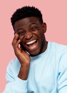 Man in light blue sweater laughing and holding his face