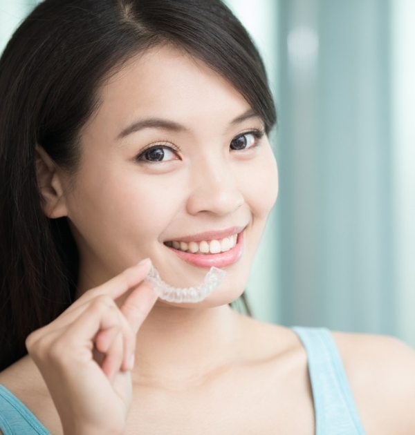 Smiling young woman holding Invisalign clear aligner