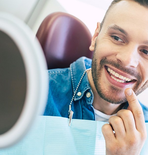 Man checking smile in mirror after teeth whitening in Hillsboro, OR