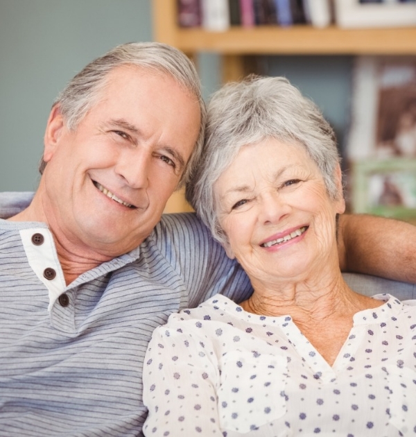 Senior man and woman smiling on couch after replacing missing teeth in Hillsboro