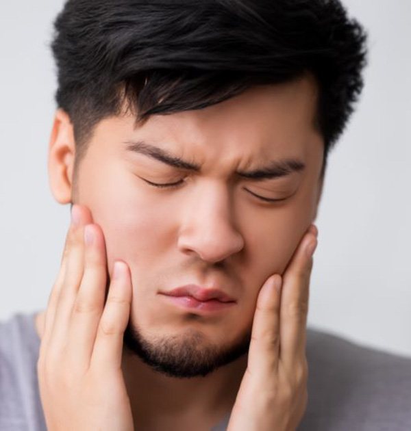 Man touching the sides of his face, suffering from TMJ disorder