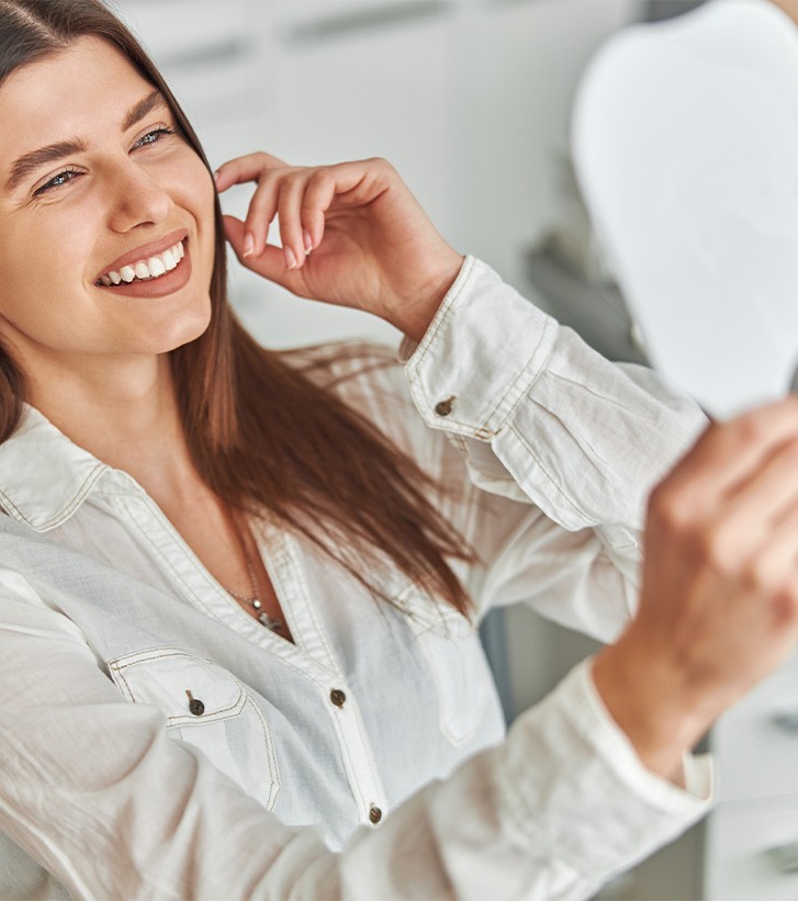Woman in button-up shirt checking smile in mirror