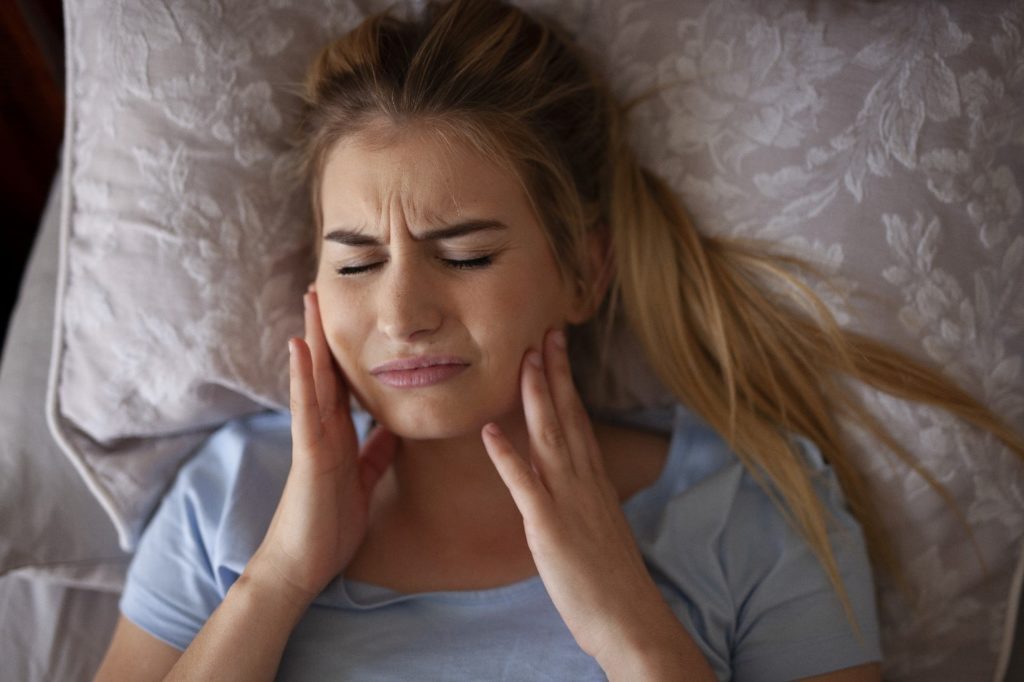 Closeup of woman experiencing jaw pain while lying in bed