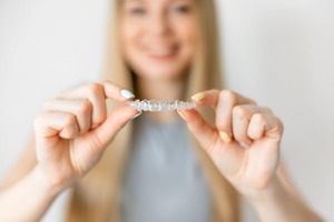 Blond woman holding up an Invisalign aligner