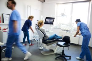 Woman in jeans and gray shirt in dentists chair looking at x-ray while 3 assistants in blue scrubs prepare