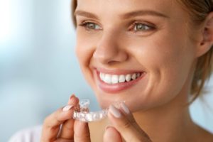 Woman with hazel eyes smiling and holding Invisalign
